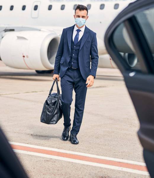 Successful businessman wearing a facial mask walking towards a car